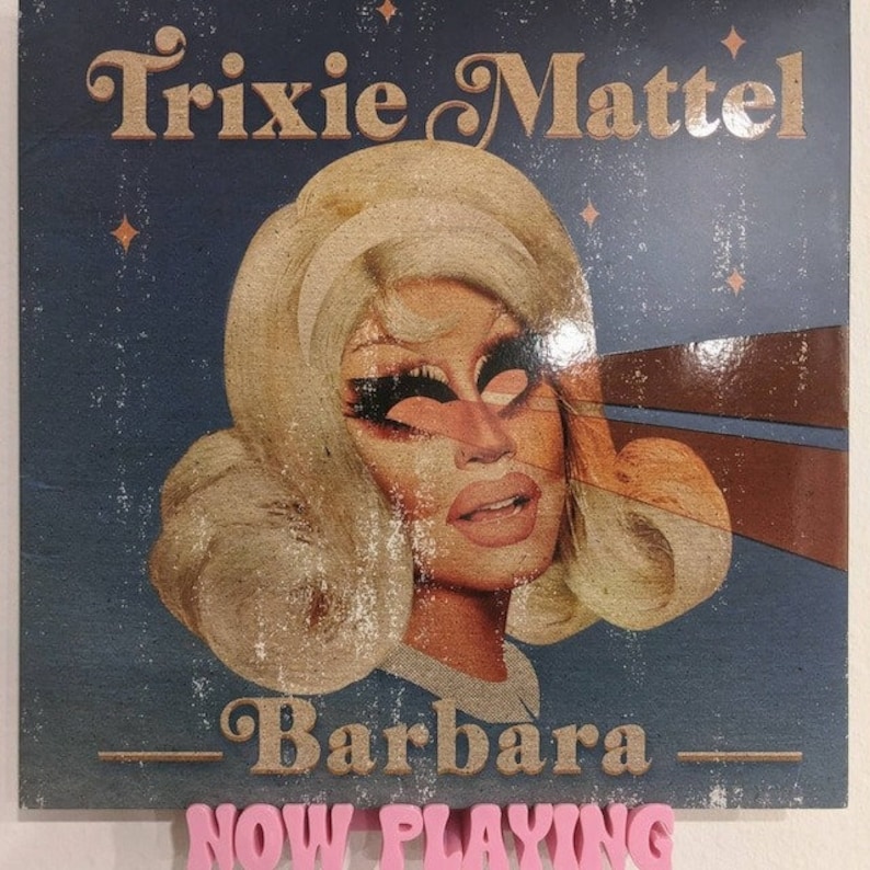 May include: A vintage-style album cover featuring a portrait of Trixie Mattel, a drag queen, with the text "Trixie Mattel" and "Barbara" in a retro font. The album cover has a blue background with stars and a brown and gold design.