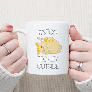 May include: White ceramic mug with a cartoon cat and the text "It's too peopley outside".