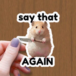 Può includere: Un adesivo con un criceto dei cartoni animati che tiene un coltello con il testo "say that again" sopra il criceto e "AGAIN" sotto il criceto.