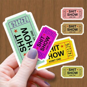 以下が含まれることがあります： さまざまな色のチケット型のステッカーのコレクションです。「SHIT SHOW」と「ADMIT ONE」のテキストが太字で表示され、星のグラフィックが付いています。チケットの色は、緑、ピンク、黄色、茶色などです。