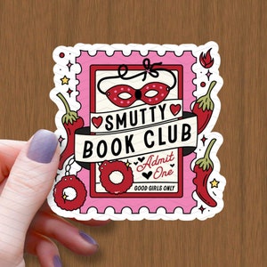 以下が含まれることがあります： ピンクと赤のステッカーに「SMUTTY BOOK CLUB」の文字と水玉模様の赤いマスクが描かれています。ステッカーには、赤い唐辛子、赤いハート、そして「Admit One」と「Good Girls Only」の文字も書かれています。
