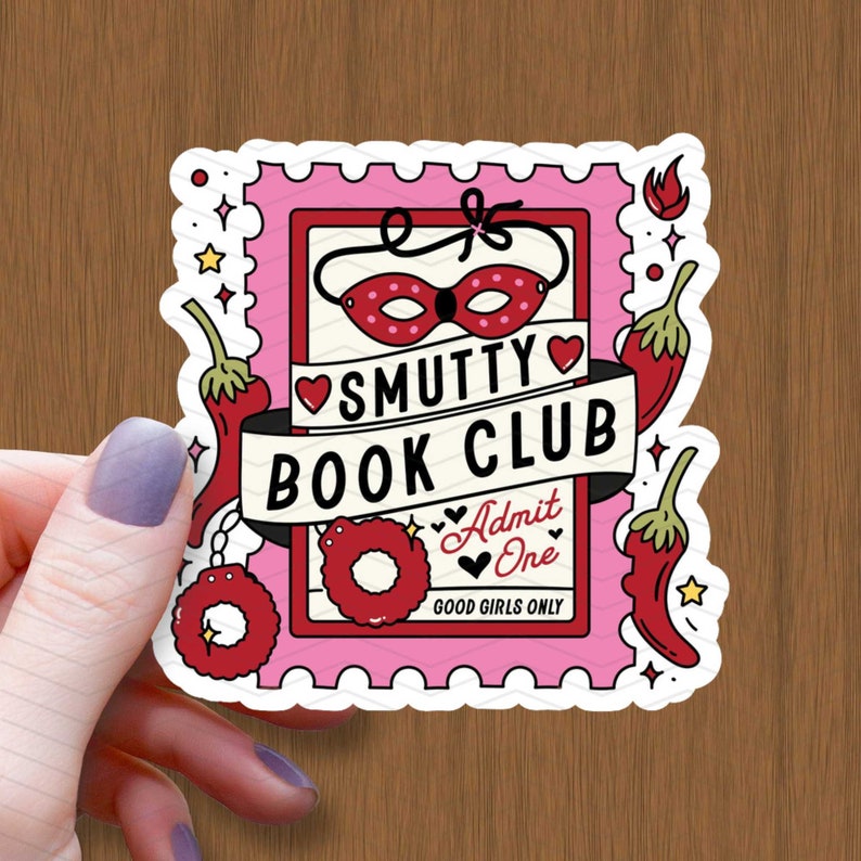 以下が含まれることがあります： ピンクと赤のステッカーに「SMUTTY BOOK CLUB」の文字と水玉模様の赤いマスクが描かれています。ステッカーには、赤い唐辛子、赤いハート、そして「Admit One」と「Good Girls Only」の文字も書かれています。