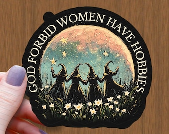 May include: A black sticker featuring the text "GOD FORBID WOMEN HAVE HOBBIES" around an illustration of four witches in black robes and hats, standing in a field of white flowers, with a moon and stars in the background.