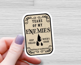 May include: A sticker with a vintage label design that reads "Tears of My Enemies" with a black and white illustration of two teardrops. The label also says "Keep Chilled, Witch's Grade, Naturally Harvested."