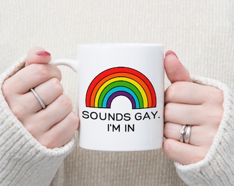 May include: White ceramic mug with a rainbow graphic and the text "SOUNDS GAY. I'M IN".