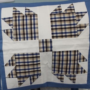 May include: A white quilt with a blue border and a plaid pattern in the center. The plaid pattern is made up of blue, brown, and white squares.