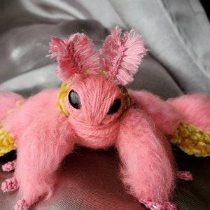 May include: A pink and yellow crocheted moth plush toy with fuzzy pink fur and yellow velvet wings.