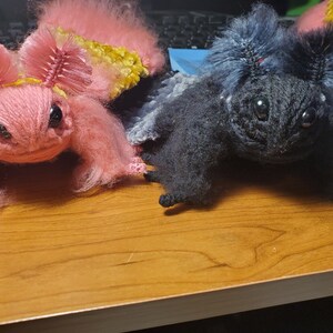 May include: Two crocheted plush toys, one pink with yellow accents and one black, with large eyes and fuzzy textures.
