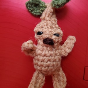 May include: A crocheted brown and green amigurumi toy shaped like a mandrake, a mythical plant with a human-like body and a leafy head.