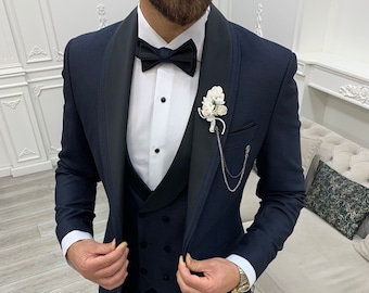 Può includere: Uno smoking blu navy con un colletto a scialle in raso nero, un papillon nero e un boutonniere di fiore bianco. Lo smoking ha un gilet abbinato con chiusura a doppio petto.