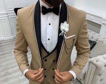 Può includere: Un abito tre pezzi color beige con revers in raso nero e papillon nero. L'abito ha un gilet con chiusura a doppio petto e un fazzoletto da taschino con una catena.