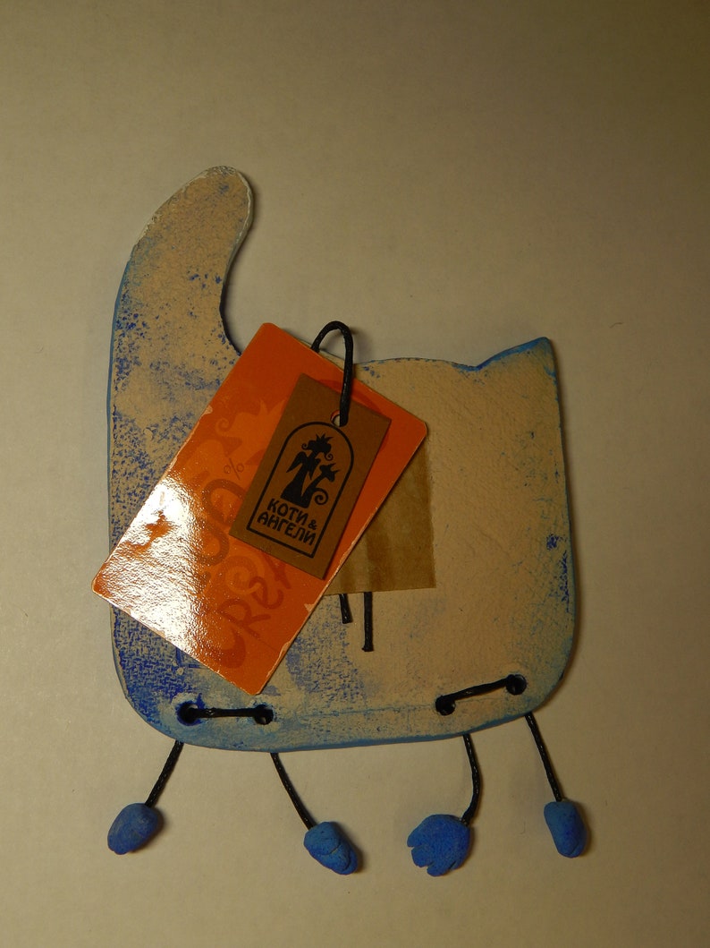 May include: A blue and white ceramic cat figurine with a tag that reads "Koti & Angeli". The cat has three legs and blue feet.