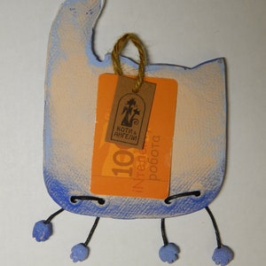 May include: A blue and white ceramic cat figurine with a tag that reads "Koti & Angeli" and "100% ręczna robota". The cat has black string legs and blue feet.