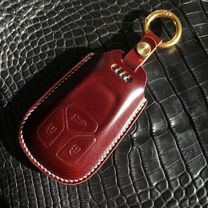 May include: A burgundy leather key fob with a white stitching detail and a gold key ring. The fob has three buttons.