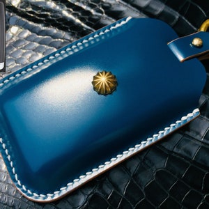 May include: A blue leather key fob with white stitching detail and a gold star-shaped button. The fob has a gold ring attached to it.