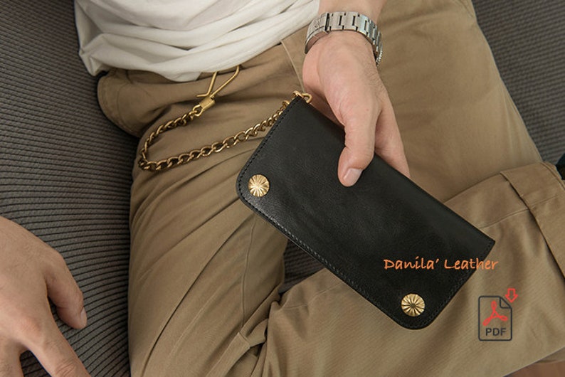 May include: A black leather wallet with a gold chain and gold accents. The wallet has the text "Danila' Leather" printed on it.