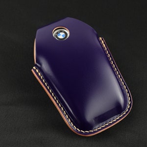 May include: A purple leather key fob with a stitched edge and the BMW logo in the centre.