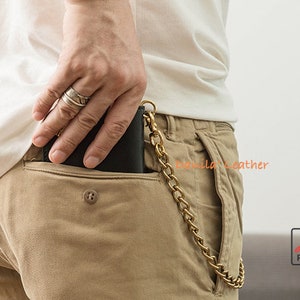May include: A black leather wallet with a brass chain attached to it. The wallet is in the back pocket of a pair of khaki pants.