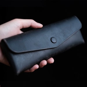 Può includere: Un astuccio per matite in pelle nera con una chiusura a bottone singolo.