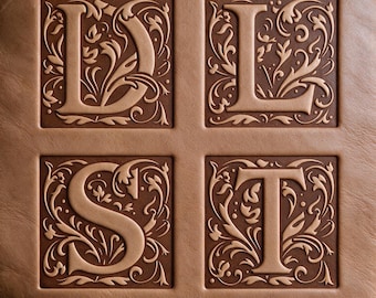 May include: A light brown leather surface featuring four square recessed panels. Each panel contains a raised, embossed letter—D, L, S, and T—surrounded by intricate, swirling floral and vine patterns in a lighter tan shade against a dark brown background.