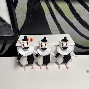 May include: Three small mouse figurines dressed as clowns, each wearing a black and white suit, a white ruffled collar, and a tiny black top hat. The mice have painted clown faces with black diamond markings around their eyes and black lips.