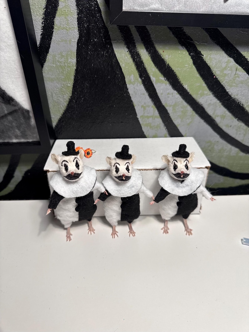 May include: Three small mouse figurines dressed as clowns, each wearing a black and white suit, a white ruffled collar, and a tiny black top hat. The mice have painted clown faces with black diamond markings around their eyes and black lips.