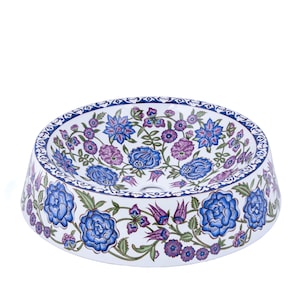 May include: A white ceramic sink with a floral design in shades of blue, purple, and green. The sink has a round bowl and a flared base.
