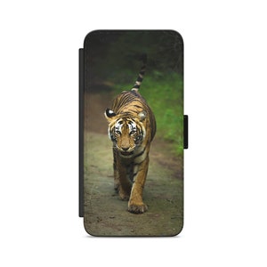 Puede incluir: Un tigre camina por un sendero a través de un exuberante bosque verde. El tigre mira directamente a la cámara con sus rayas claramente visibles.