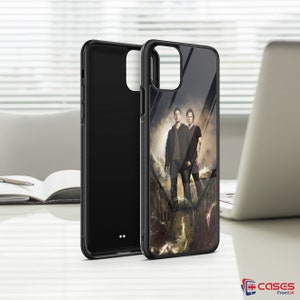 May include: Black phone case with a clear back showing a photo of two men standing in front of a dark background. The men are wearing casual clothing and are looking at the camera.