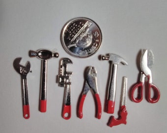 May include: A set of miniature tools with red handles, including a hammer, wrench, pliers, and a saw. The tools are arranged on a white surface with a Canadian coin in the background.