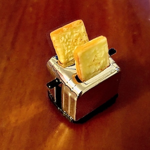 Op de afbeelding: Een miniatuur zilveren broodrooster met twee sneetjes geroosterd brood erin.
