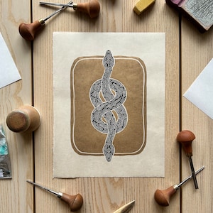 Op de afbeelding: Een zwart-witte lijntekening van een slang die in een figuur acht is geknoopt. De tekening is op een bruine papieren achtergrond en wordt omlijst door een witte rand.