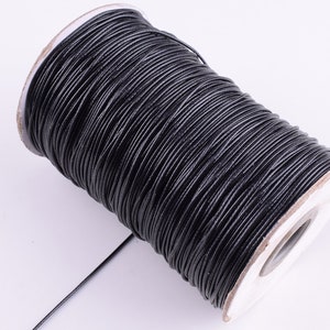 May include: A spool of black leather cord, wound tightly around a white cardboard core.