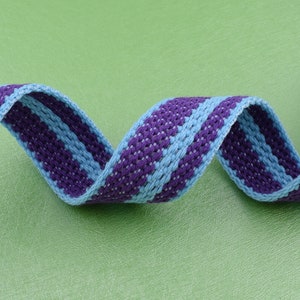 May include: A close-up of a blue and purple striped woven webbing. The webbing is twisted and curled, showing the texture of the fabric.