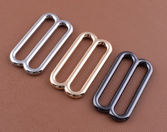 May include: Three metal slider buckles in different finishes: silver, gold, and black. Each buckle has two loops.