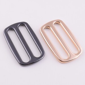 May include: Two metal slider buckles, one in black and one in gold. The buckles are rectangular with two parallel slots.