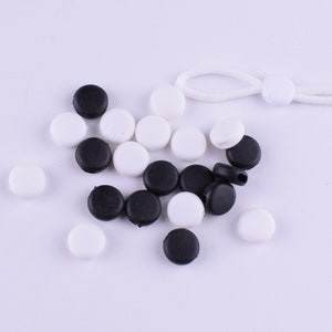 May include: A collection of black and white round plastic stoppers. The stoppers are arranged in a random pattern on a white surface.