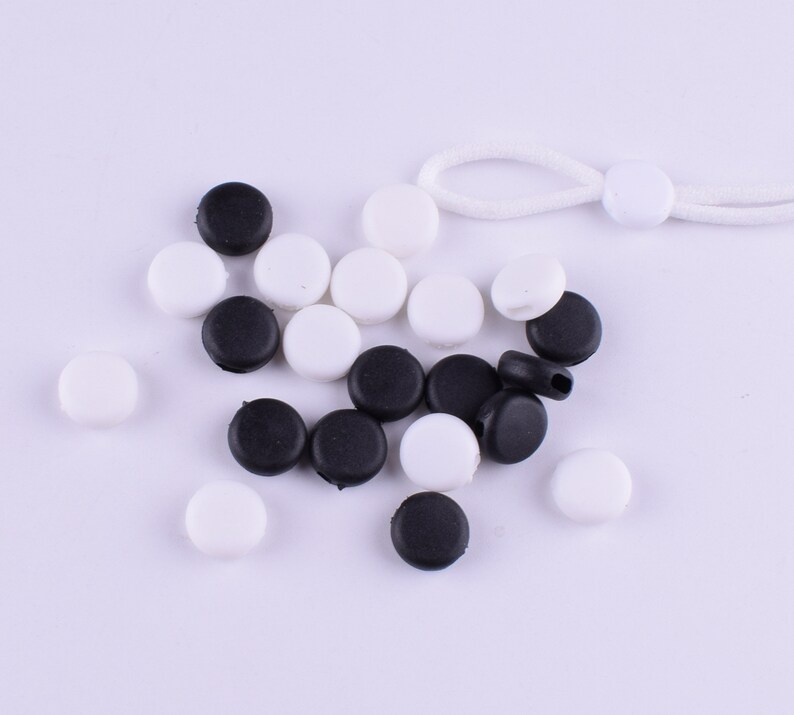 May include: A collection of black and white round plastic stoppers. The stoppers are arranged in a random pattern on a white surface.