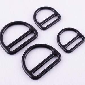 Pode incluir: Três argolas em D de metal preto de diferentes tamanhos. As argolas são lisas e têm um acabamento polido.