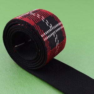 May include: Red, black, and white plaid elastic webbing rolled up. The webbing is black on the underside.
