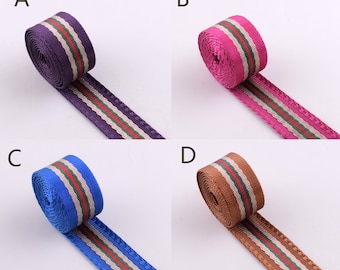 Pode incluir: Quatro rolos de fita de tecido listrada em diferentes cores: roxo, rosa, azul e marrom. Cada rolo tem uma faixa branca, uma faixa verde e uma faixa vermelha.