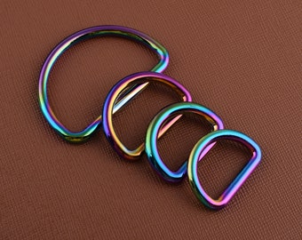 May include: Four iridescent D-rings in varying sizes, arranged diagonally on a brown surface. The rings display a spectrum of colors, including blues, greens, purples, and yellows, creating a vibrant, eye-catching effect. These metal rings are likely used for crafting or hardware.