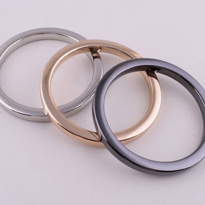 May include: Three metal rings in different finishes: silver, gold, and black. The rings are interlocked, creating a decorative design.