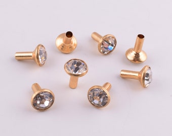 May include: Eight gold-toned metal studs with clear rhinestone accents. The studs have a round base and a pointed top.