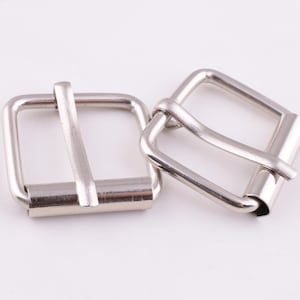 May include: Two silver metal belt buckles. The buckles are rectangular with a smooth, polished finish. They have a simple, classic design.