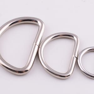 May include: Three silver metal D-rings of different sizes. The largest ring is about 5 cm in diameter, the middle ring is about 4 cm in diameter, and the smallest ring is about 2.5 cm in diameter.