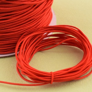 May include: A spool of bright red elastic cord. The cord is tightly wound on a cardboard spool, with a small length of cord unwound and looped. The color is a vibrant, solid red.