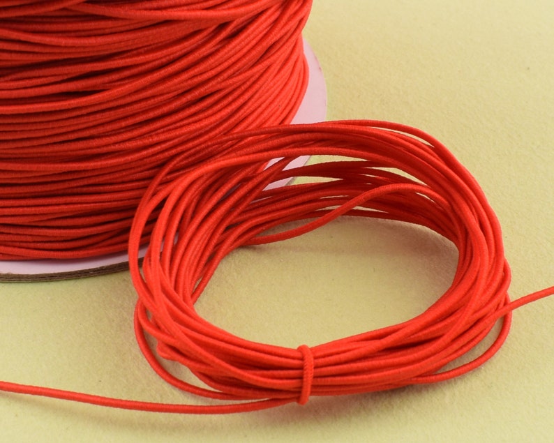 May include: A spool of bright red elastic cord. The cord is tightly wound on a cardboard spool, with a small length of cord unwound and looped. The color is a vibrant, solid red.