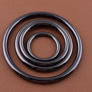 K&ouml;nnte beinhalten: Vier schwarze Metallringe in verschiedenen Gr&ouml;&szlig;en, ineinander verschachtelt. Die Ringe sind glatt und gl&auml;nzend, mit einer leicht abgerundeten Kante.