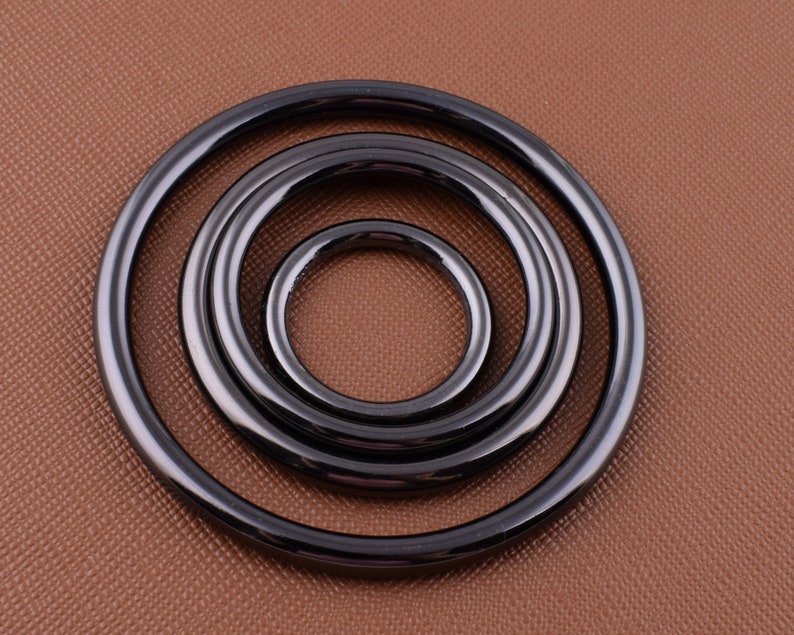 K&ouml;nnte beinhalten: Vier schwarze Metallringe in verschiedenen Gr&ouml;&szlig;en, ineinander verschachtelt. Die Ringe sind glatt und gl&auml;nzend, mit einer leicht abgerundeten Kante.